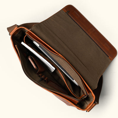 Spacious Roosevelt leather satchel in rich amber brown with secure flap and reinforced stitching.